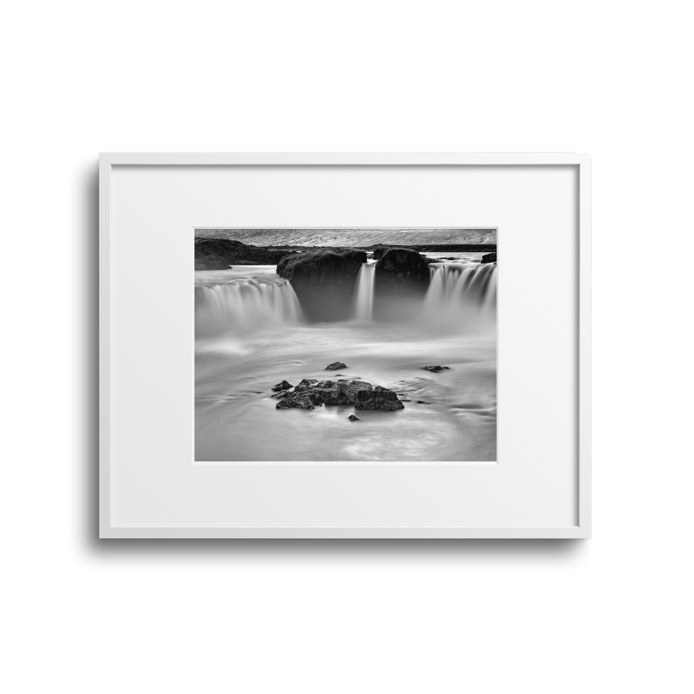 Black and white photograph of a waterfall in a natural landscape, with rocks in the foreground and flowing water over rocks in the background.