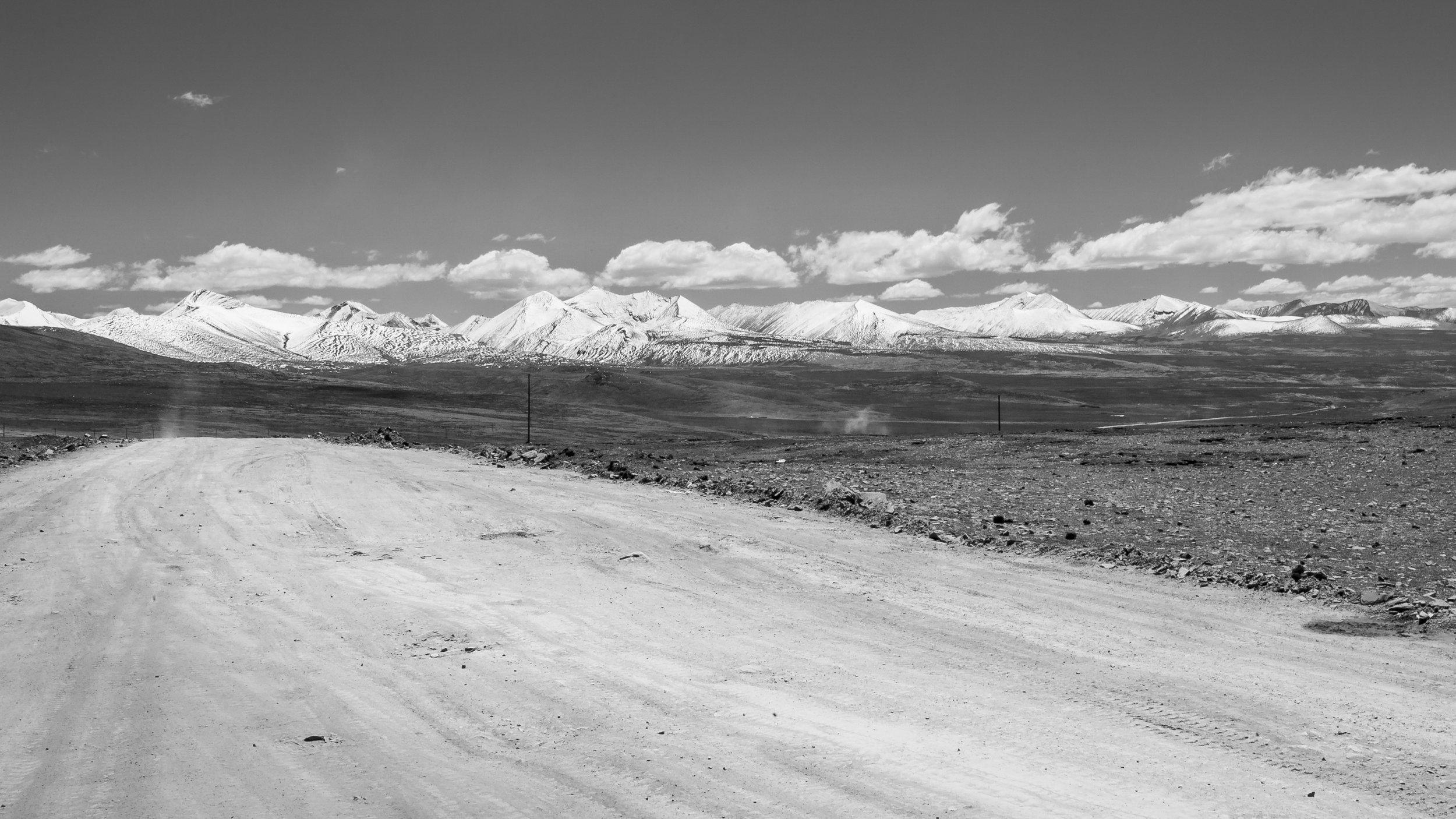 Dirt road stretching across an open plateau toward distant snow-covered mountains in Tibet.