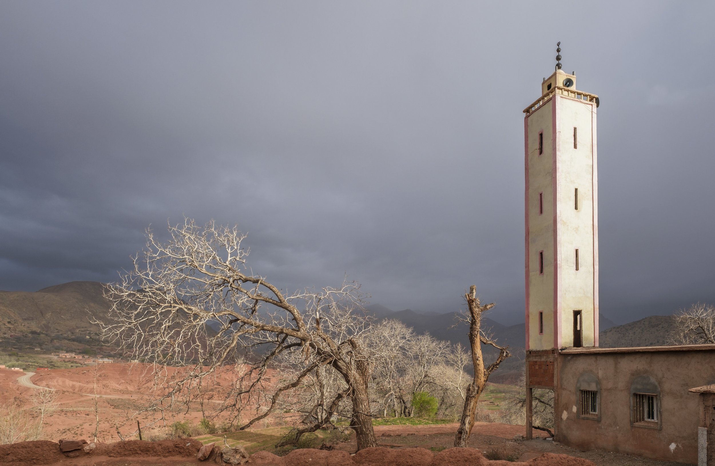 Minaret of a village mosque under dark storm clouds in Morocco’s High Atlas Mountains.