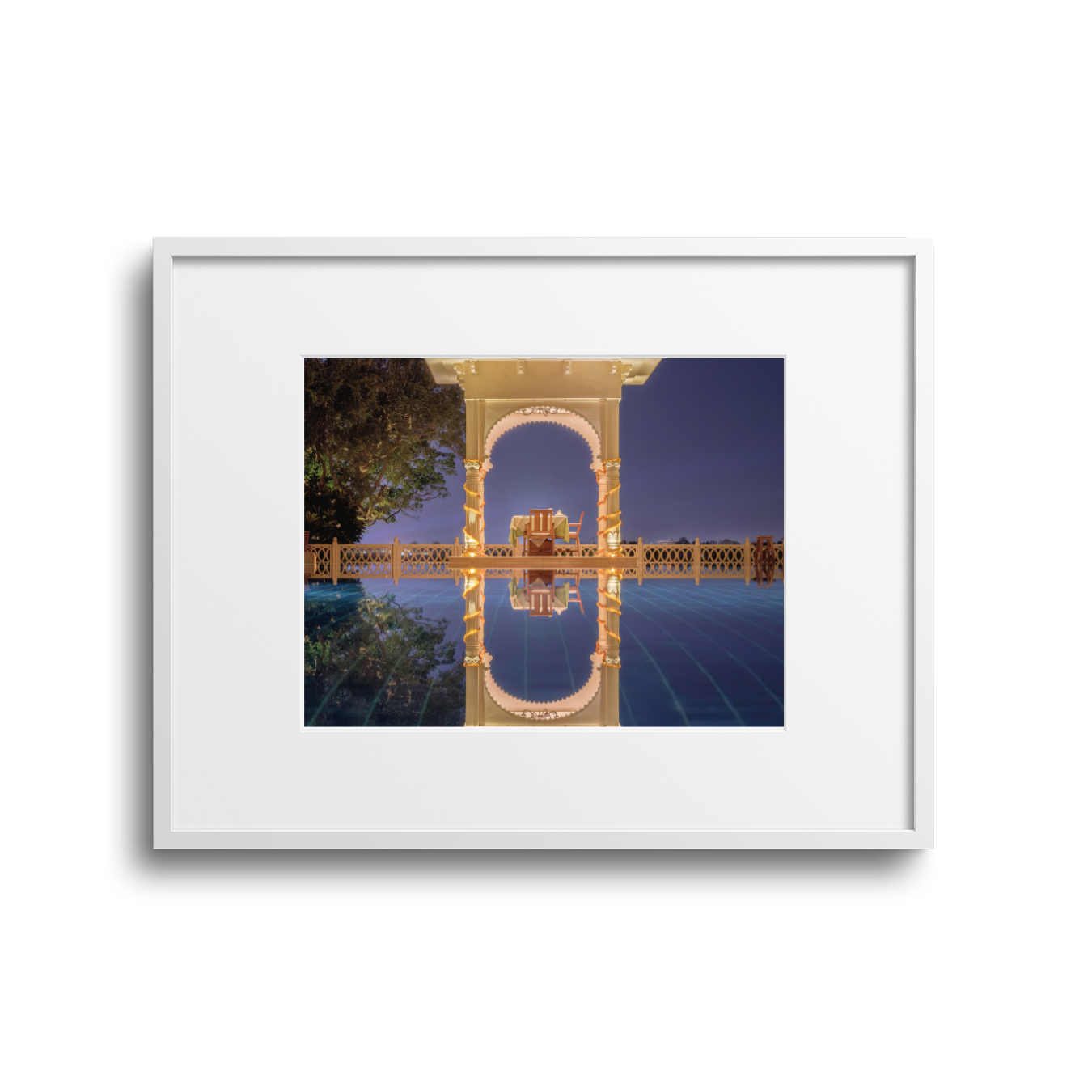 Elegant chair set on a decorated porch with arches, illuminated at night, reflected in a pool.