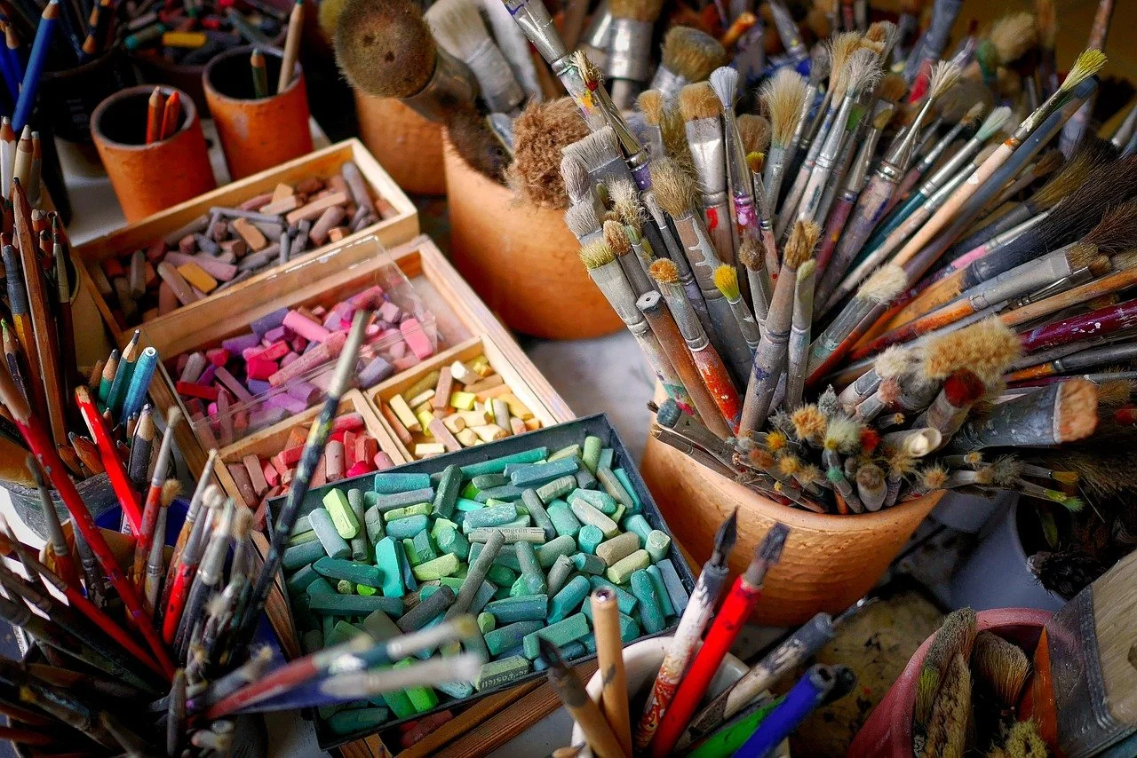 Argentiques de crayons de couleur et pinceaux de peinture disposés dans des contenants en bois et en plastique.