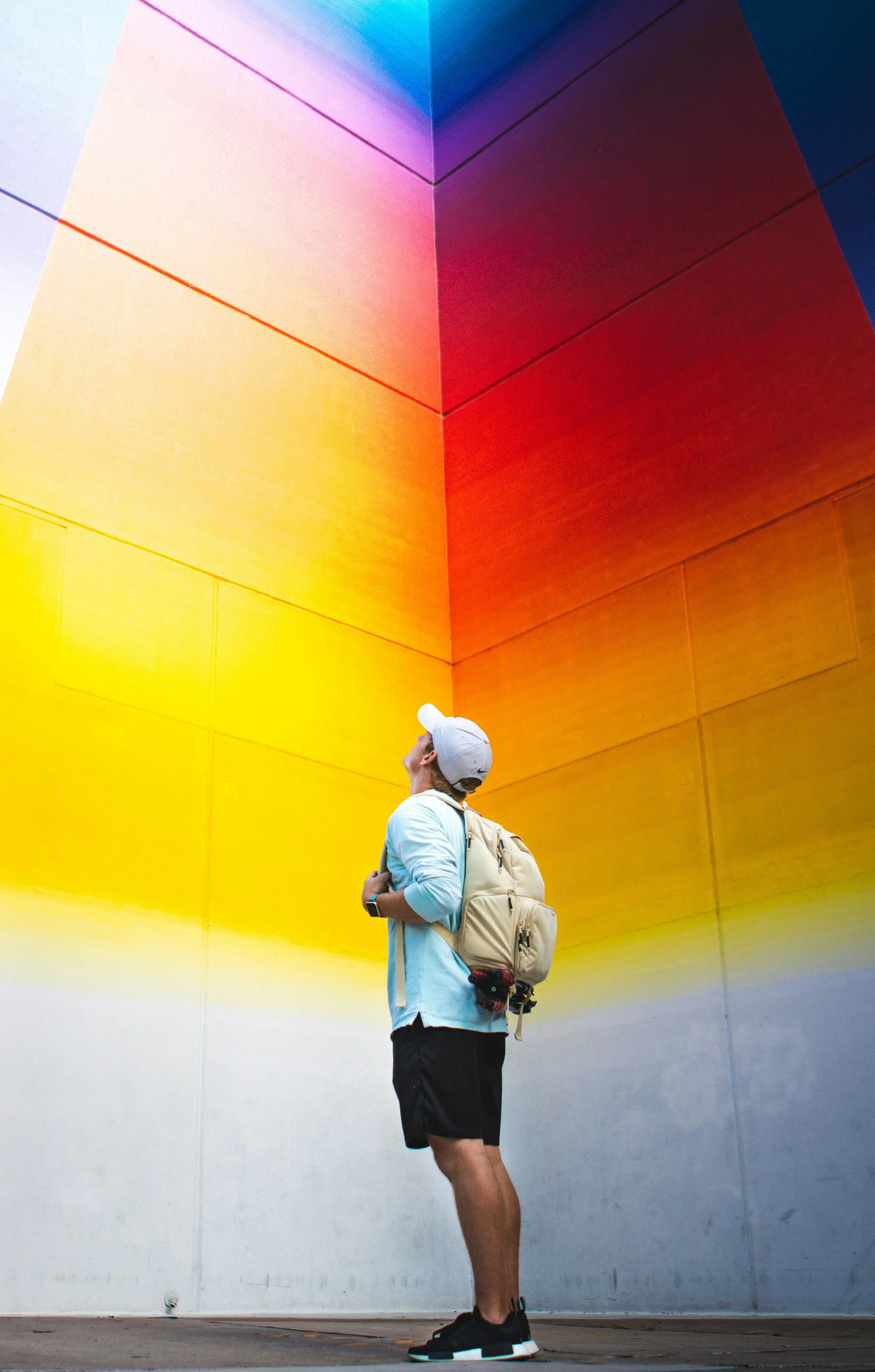 Jeune homme avec un sac à dos regardant une murale colorée avec des dégradés de jaune, orange, rouge et bleu.