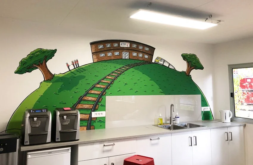 Mural illustrant une colline verte avec des arbres et des rails de train menant à un bâtiment, dans une cuisine.