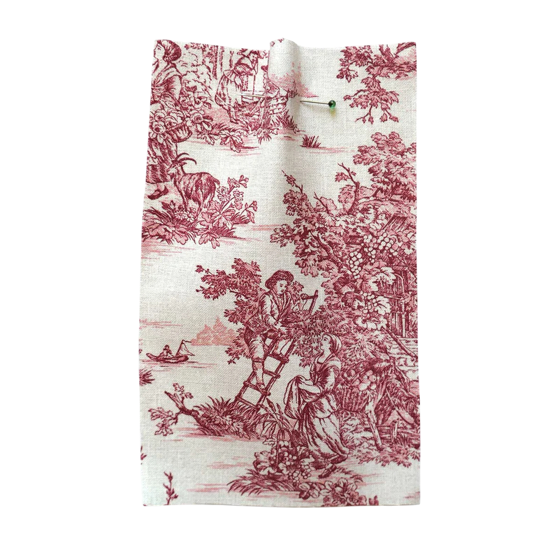 A piece of fabric with a traditional toile pattern in red and white, depicting people, trees, wildlife, and a scenic landscape.