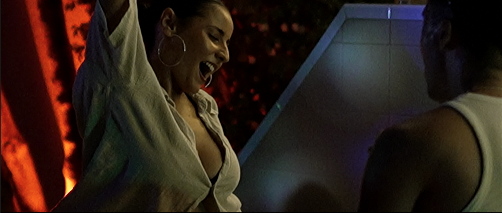 Dos mujeres riendo y conversando en un espacio con iluminación ambiental de colores oscuros y fondo con luces rojas y azules.