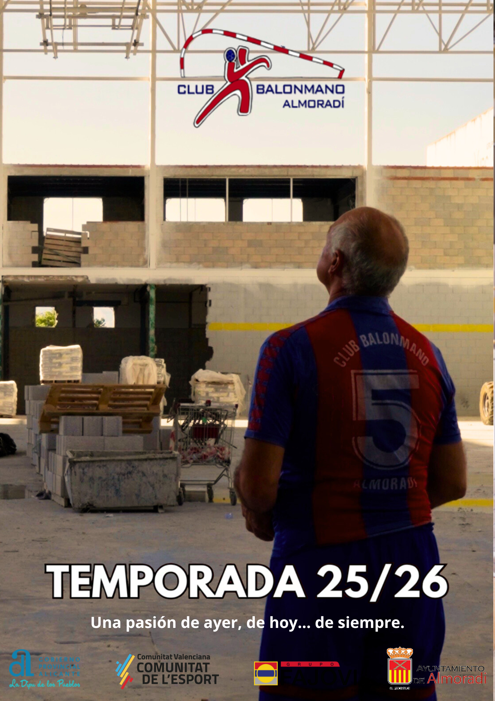 Hombre con camiseta de club de balonmano en un almacén, mirando un cartel con el logo y el nombre del club, en una construcción en proceso.