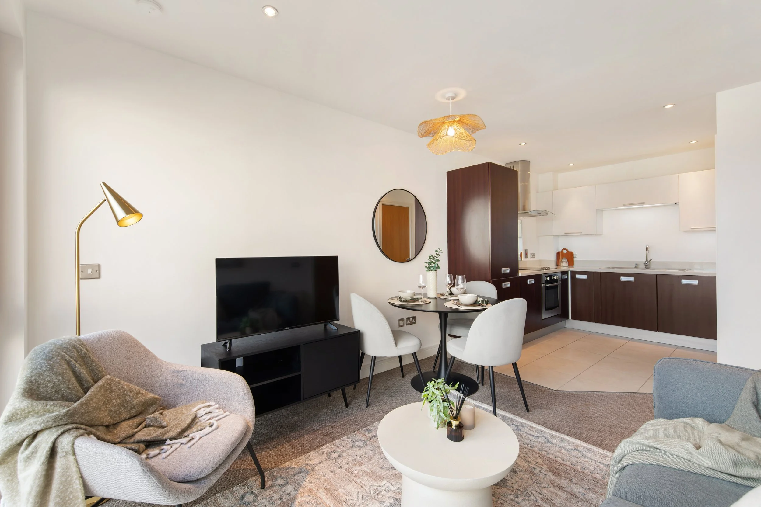 Open plan living room and kitchen with modern furniture, a flat-screen TV, dining table with four white chairs, and kitchen with dark and white cabinetry.