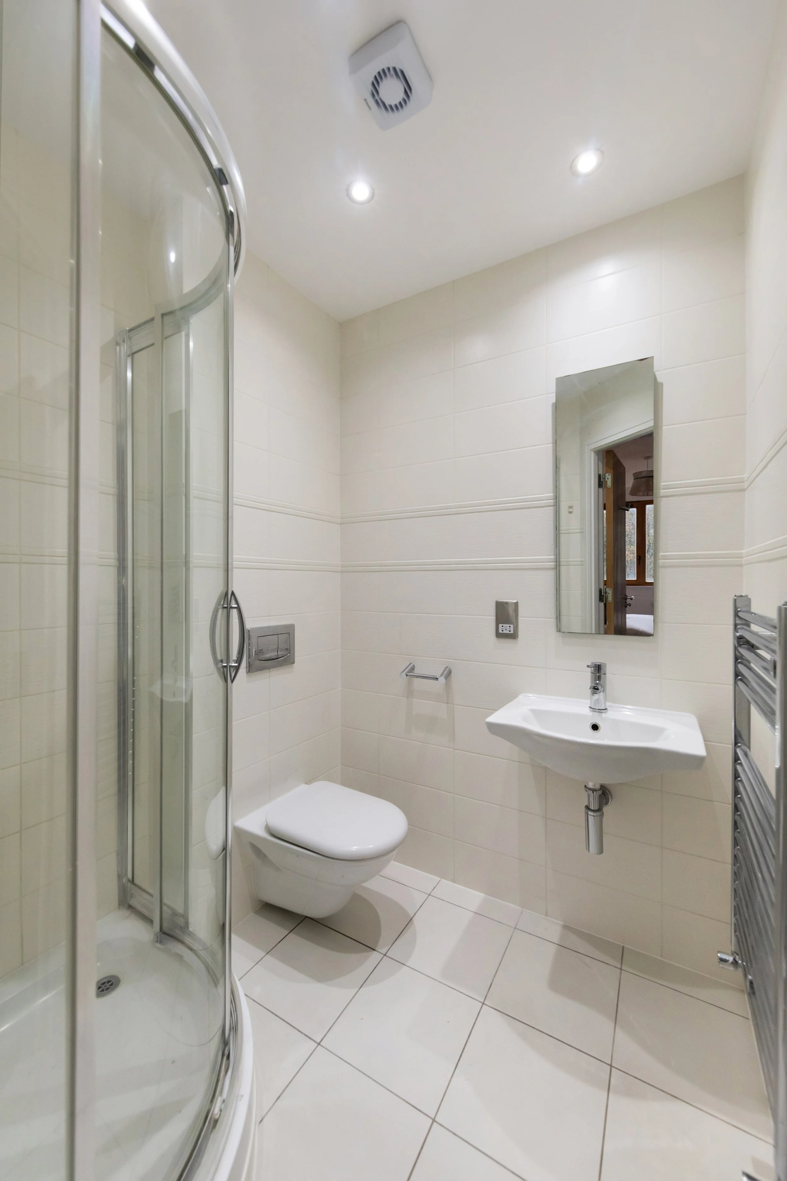 Minimalist bathroom with a glass corner shower, wall-mounted toilet, small wall-mounted sink, mirror, and heated towel rail.