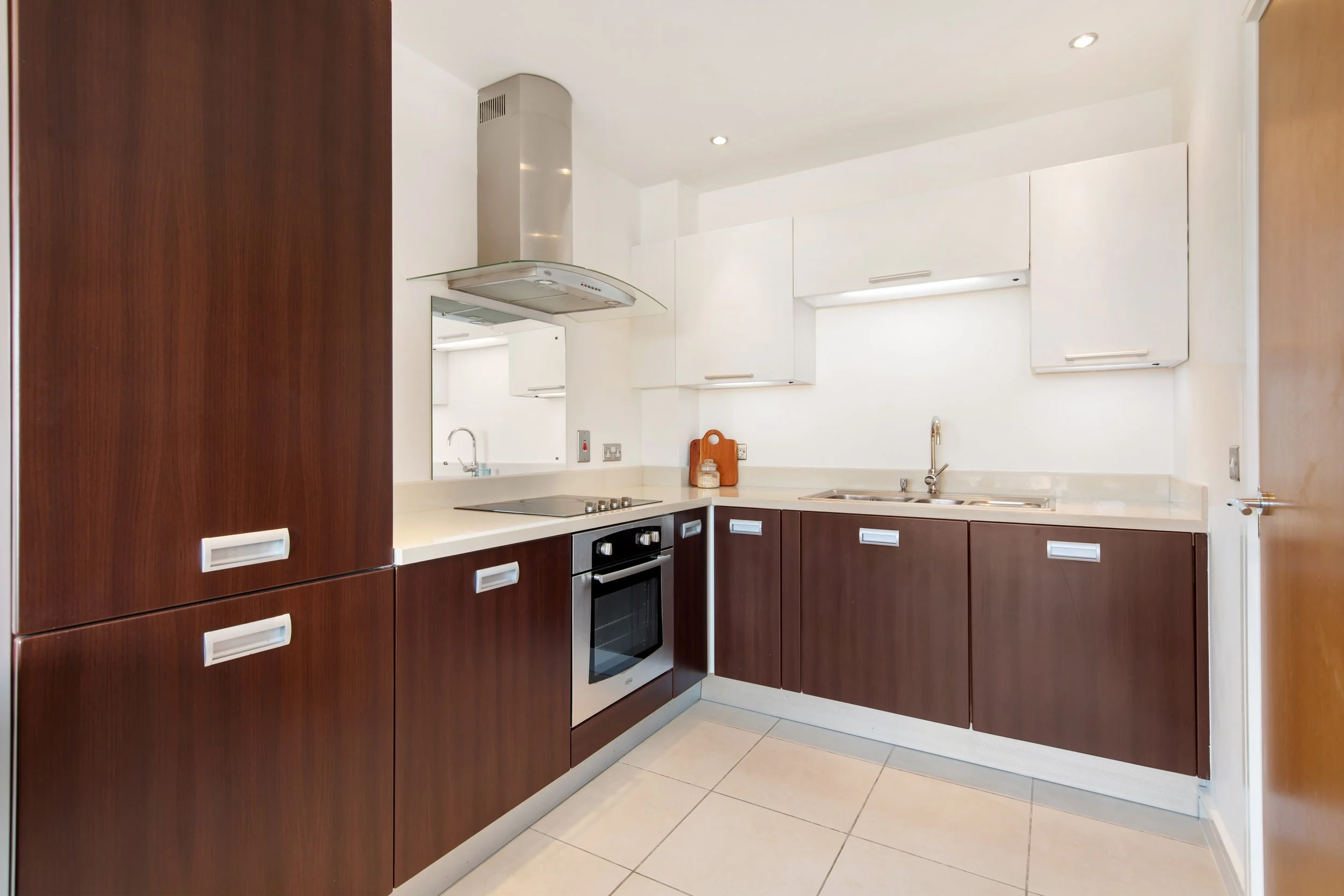 Modern kitchen with dark brown lower cabinets, white upper cabinets, beige countertops, built-in oven, stovetop, and stainless steel sink.