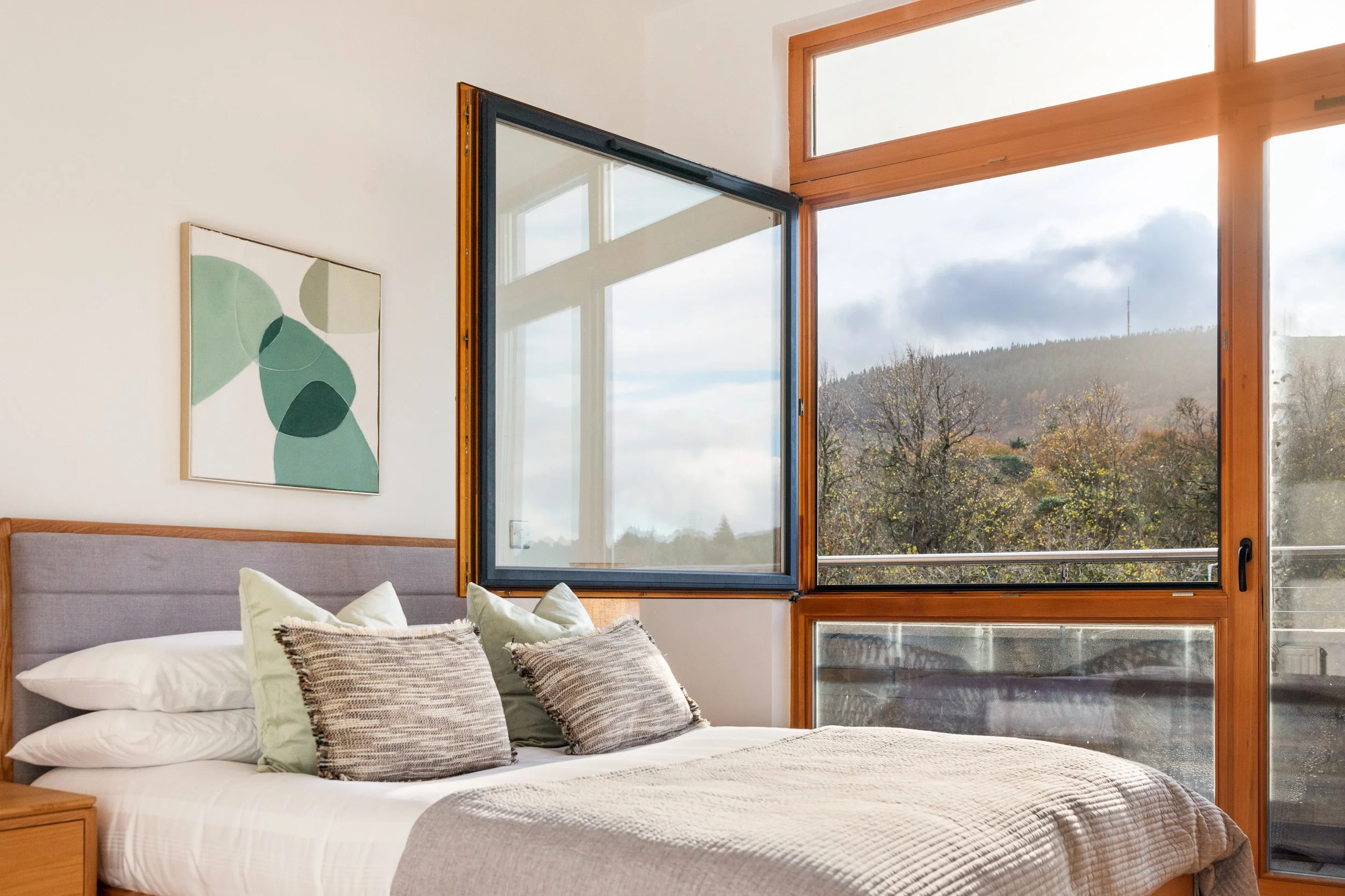 Bedroom with a bed, pillows, and a large window showing a view of trees and a scenic landscape.