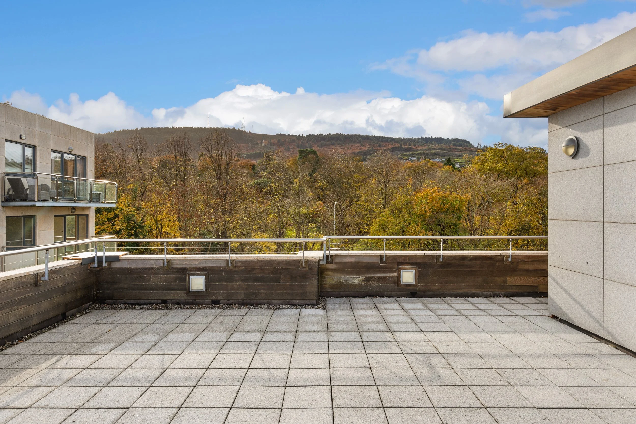 Empty rooftop terrace with view of trees and hills under blue sky with clouds