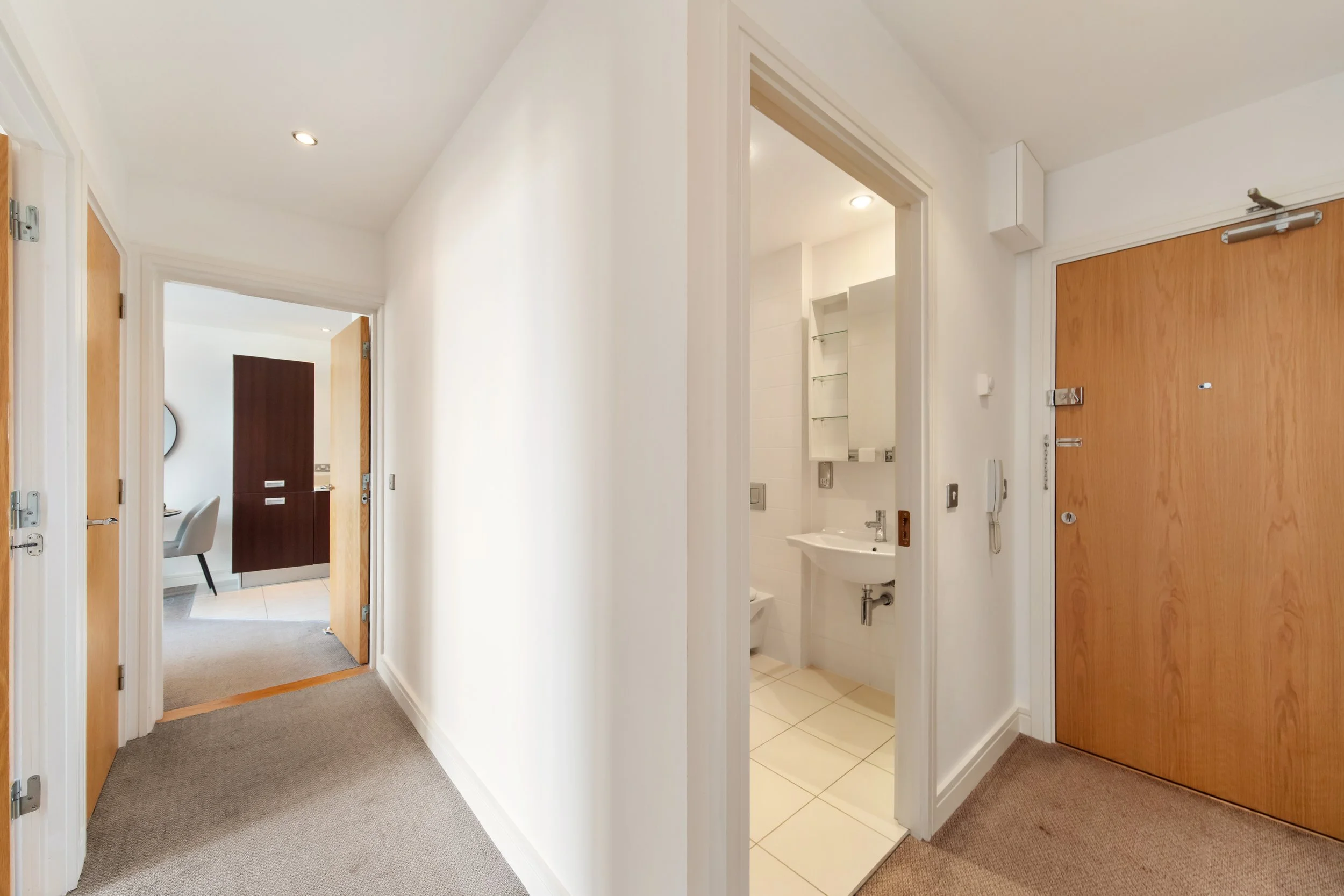 Hallway with visible doors leading to rooms and a bathroom with white tiles and fixtures.