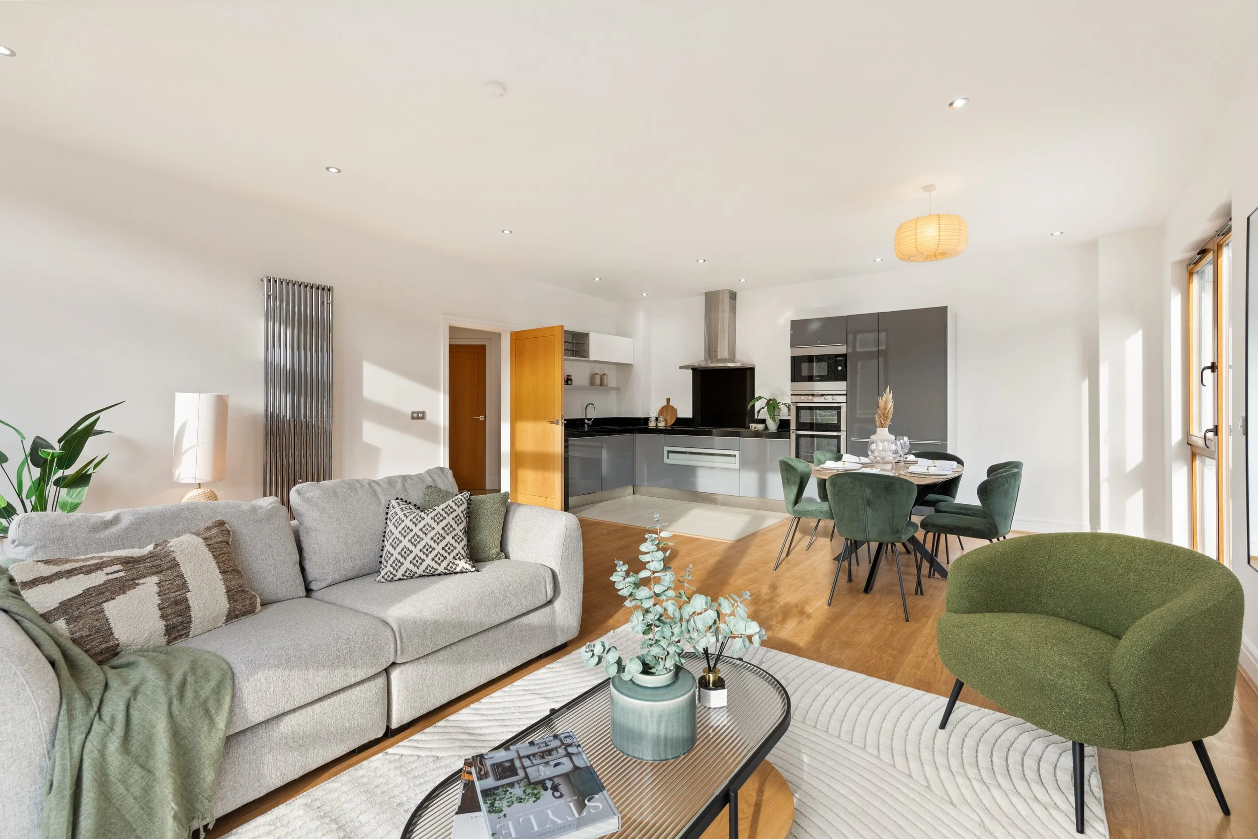 Open concept living room and kitchen with greenery and modern furniture.