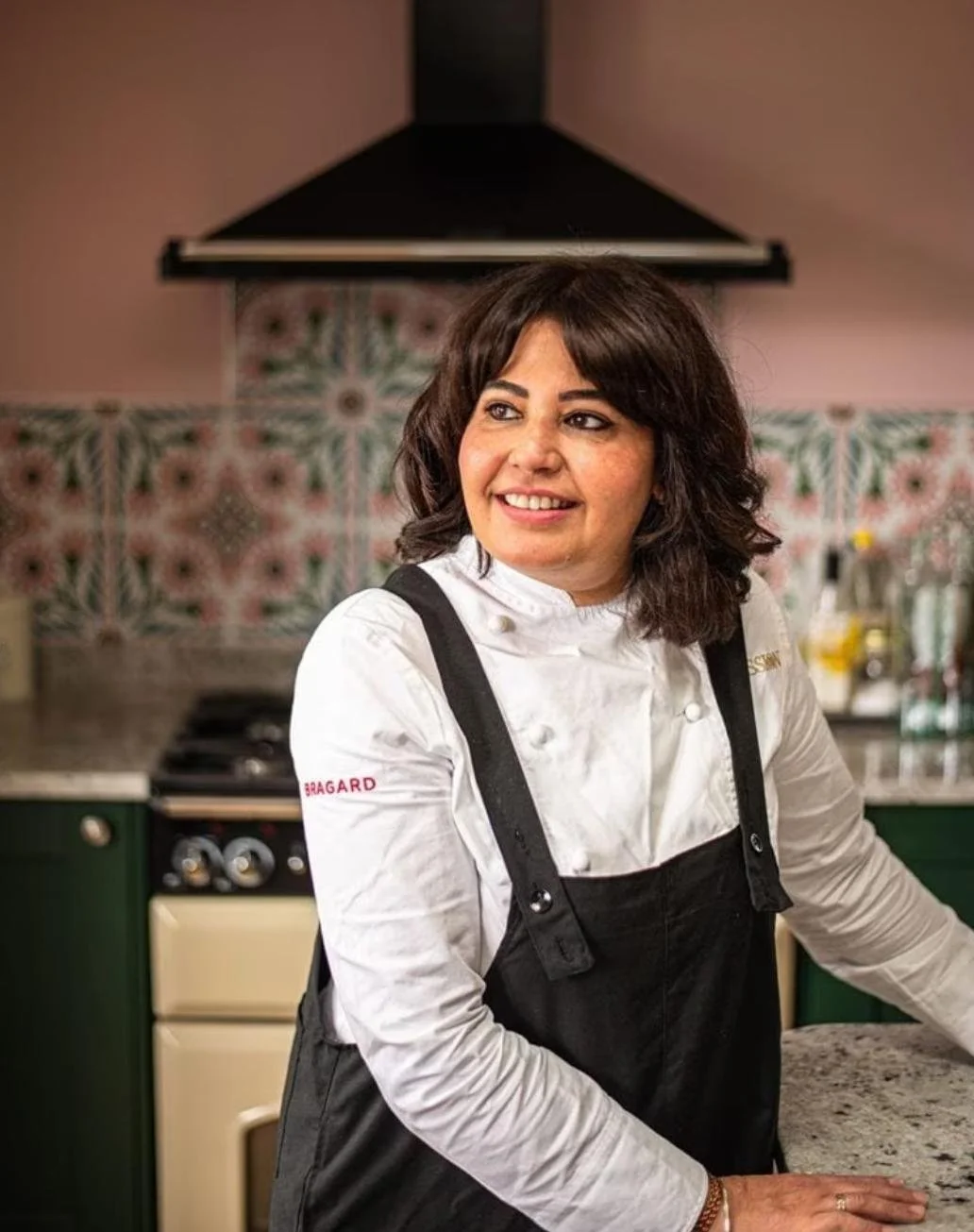 Female chef in white shirt and black apron in a colorful kitchen.