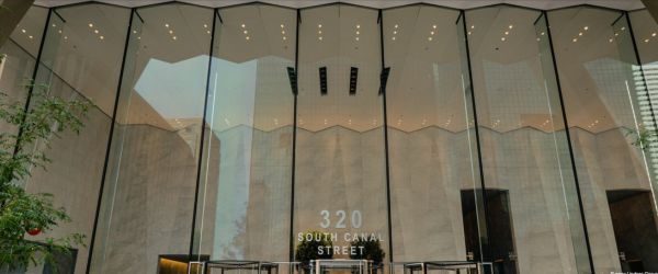 The entrance of a modern building with large glass panels and a sign reading '320 South Canal Street' at the front.