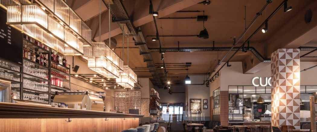 Interior of a modern restaurant or cafe with a bar area, decorative lighting, and seating.