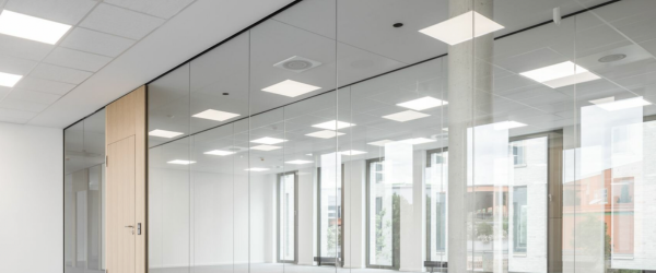Empty modern office space with glass walls and ceiling lights.