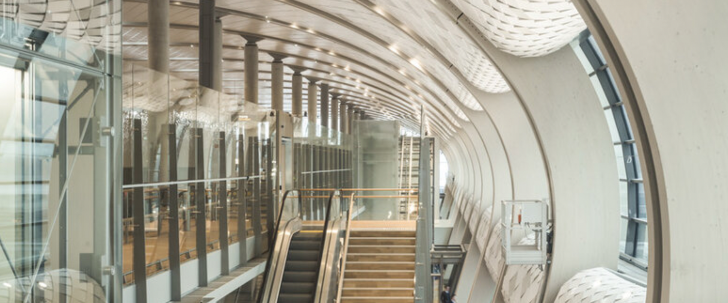 Interior view of a modern building with curved architectural design, glass walls, and escalators.