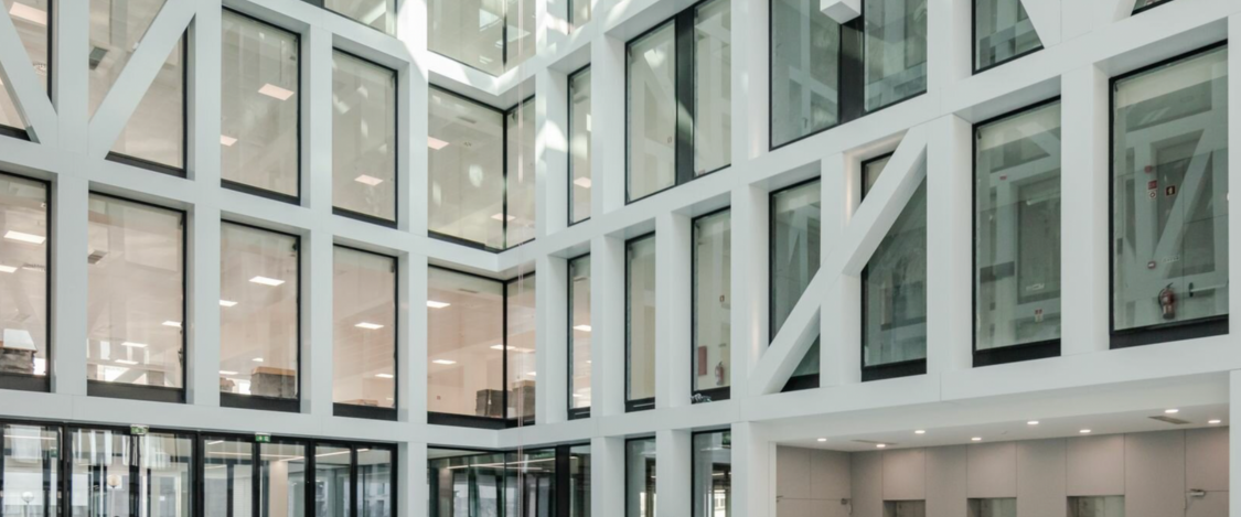 Modern office building interior with large glass windows and white structural framing.
