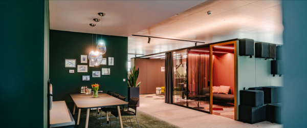 Modern office interior with a conference table, artwork on the wall, seating area with curtains, and a small lounge space with sofa and hanging lights.