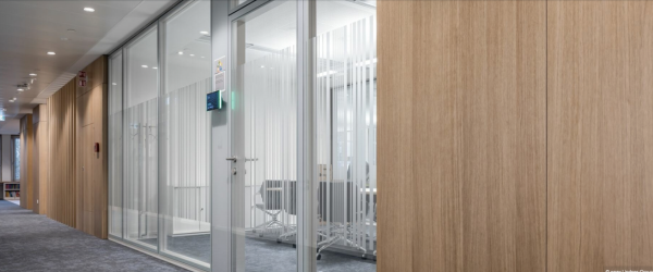 Modern office interior with glass walls, a conference room, and wooden paneling.