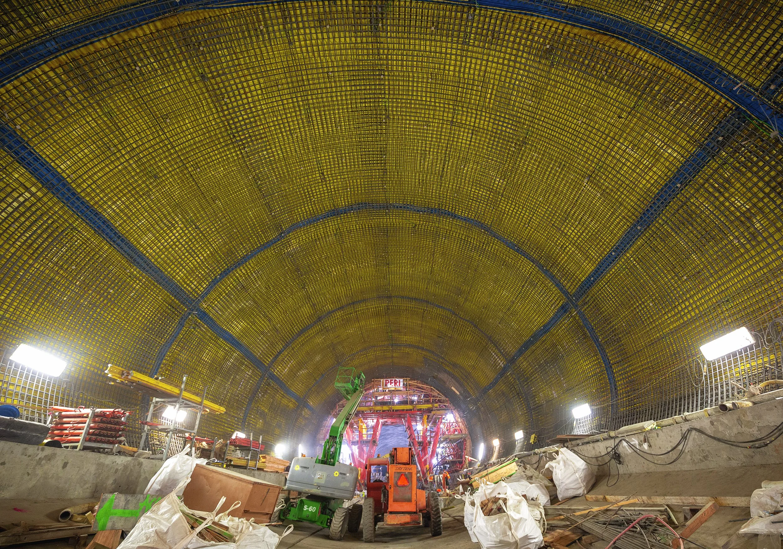 Construction workers inside a tunnel with scaffolding, equipment, and lighting, working on the tunnel's interior structure.
