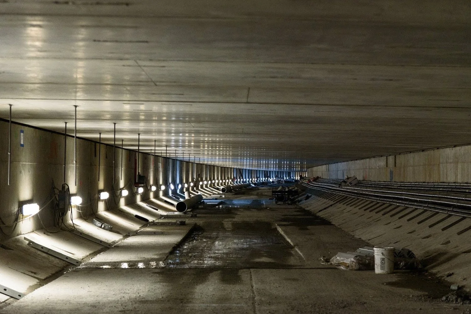 Underground construction site with pipes, construction lights, and tracks for a subway or train station.
