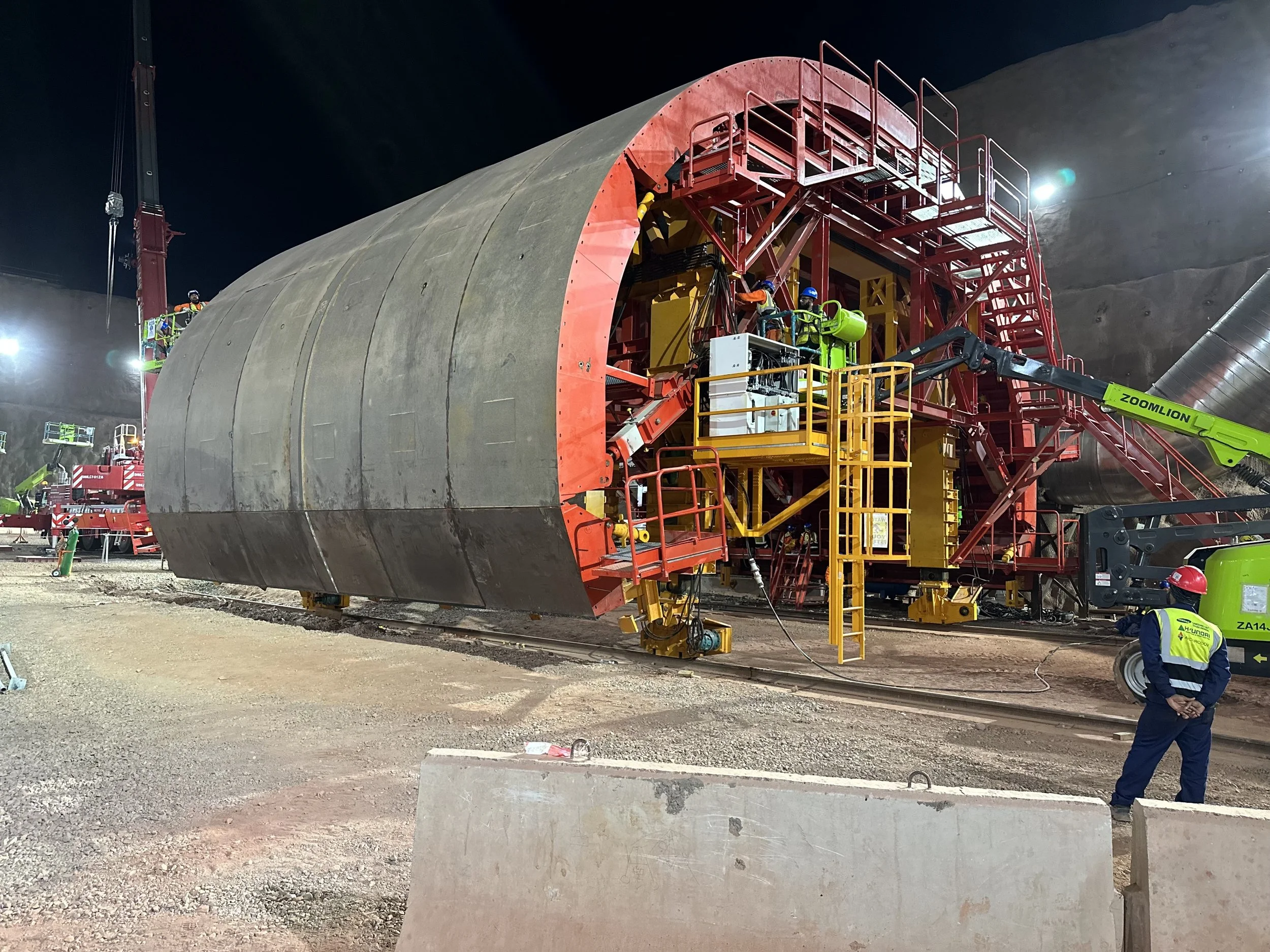 Nighttime construction scene with workers inspecting a large tunnel boring machine.