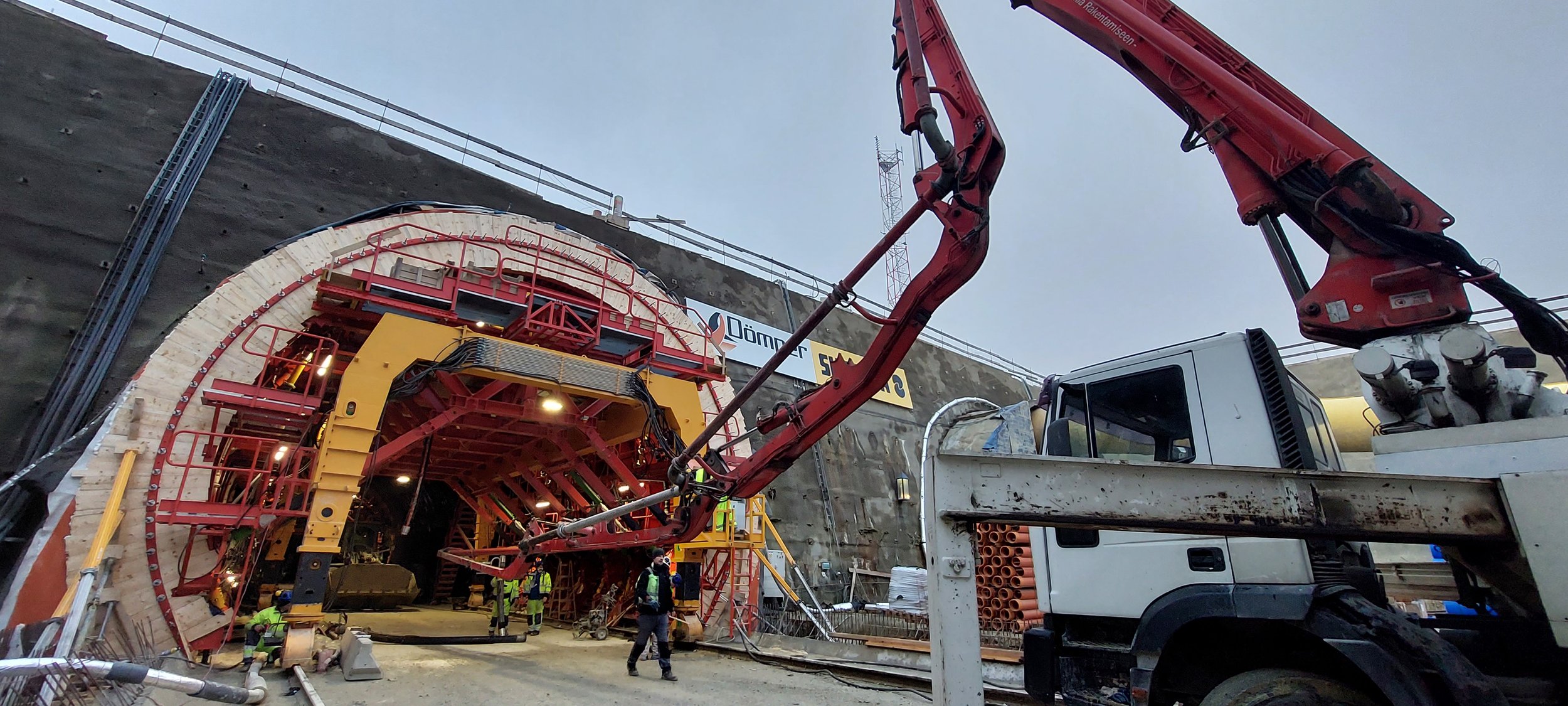 Construction workers are building a large tunnel with the help of a crane and concrete machinery.