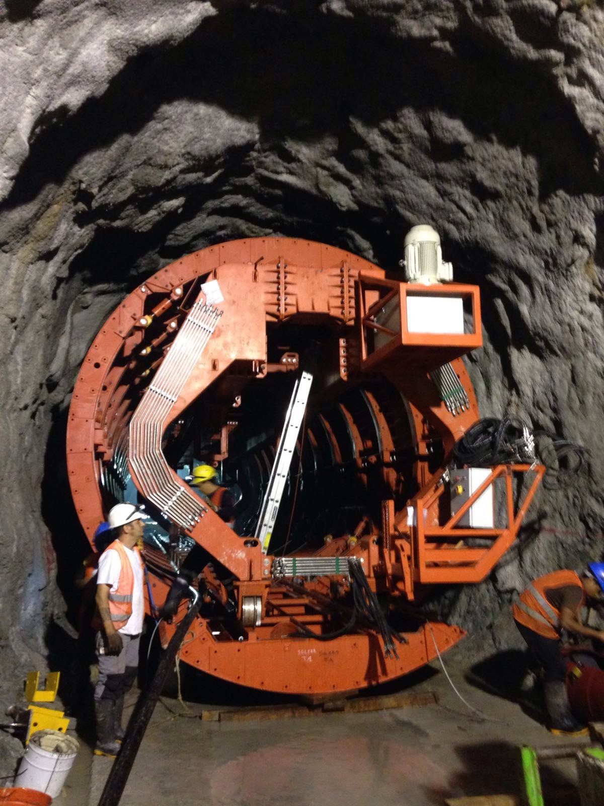 Workers in safety gear operate a large tunnel boring machine inside a deep underground passage.