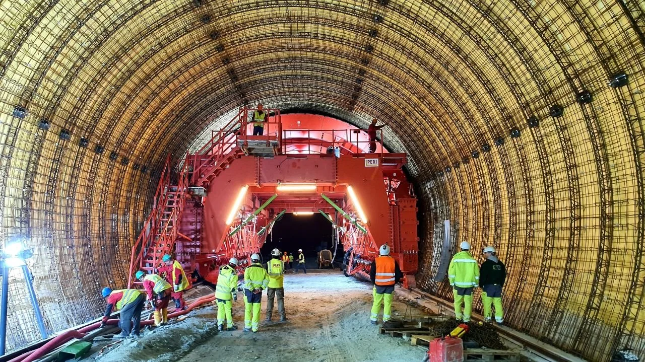 Construction workers in safety gear working inside a large tunnel with a red tunnel boring machine.