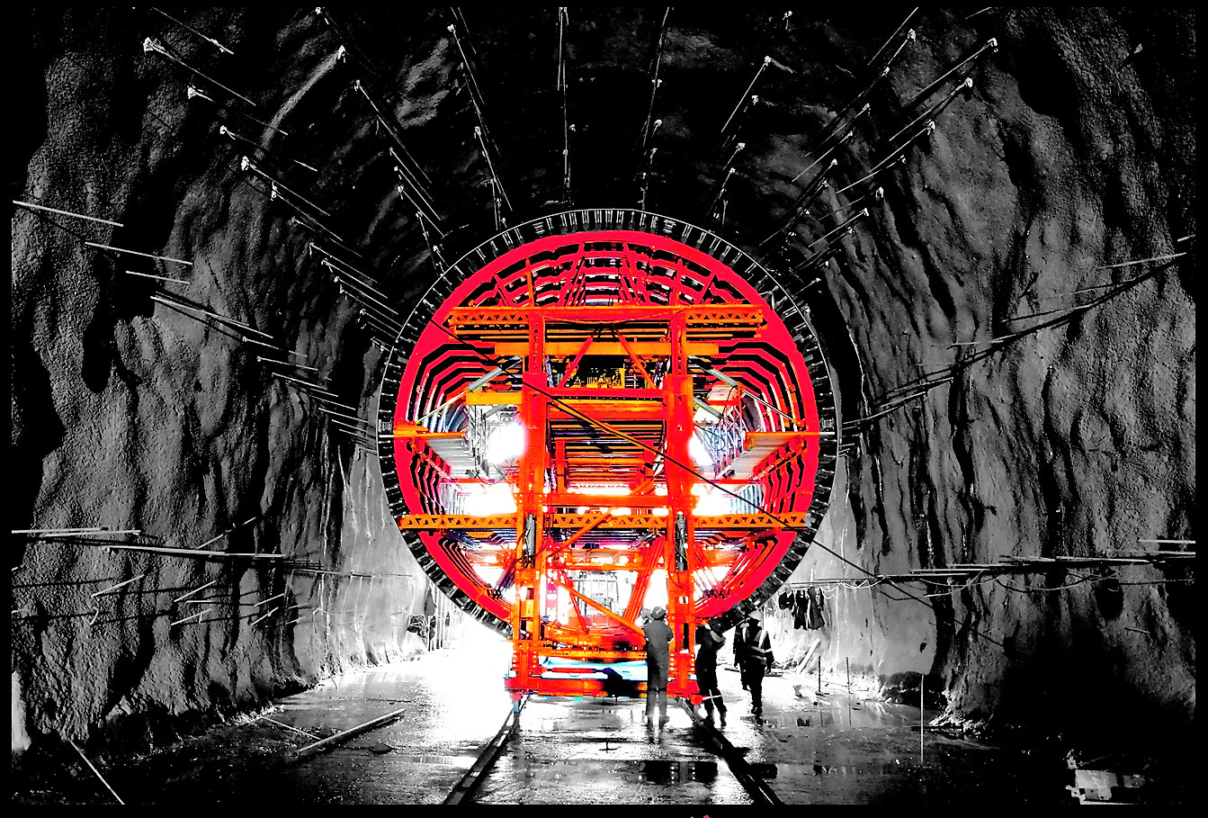 Construction workers inside a tunnel with a large, illuminated red and orange tunnel boring machine