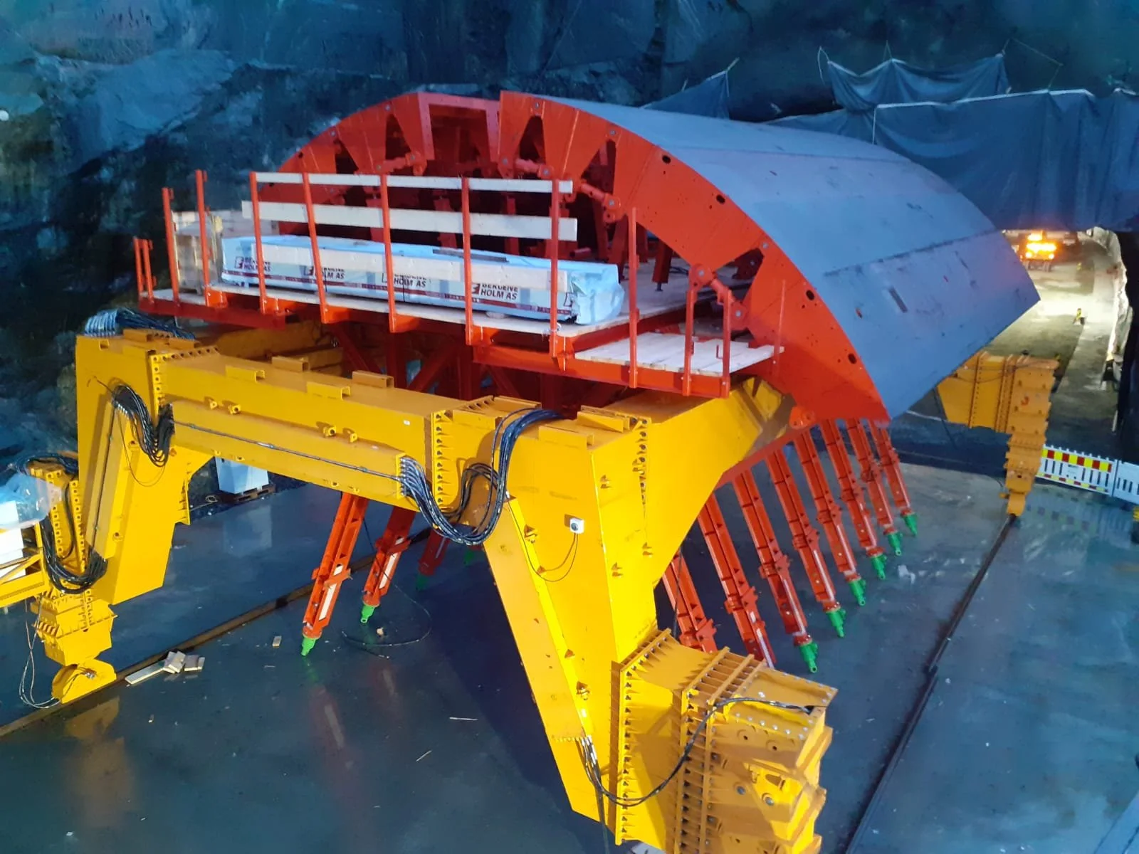 Large industrial tunnel boring machine with a yellow and orange exterior in a construction site.