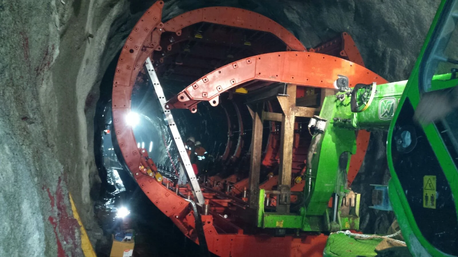 Underground tunnel construction with large red and black tunnel boring machine and workers with safety gear.