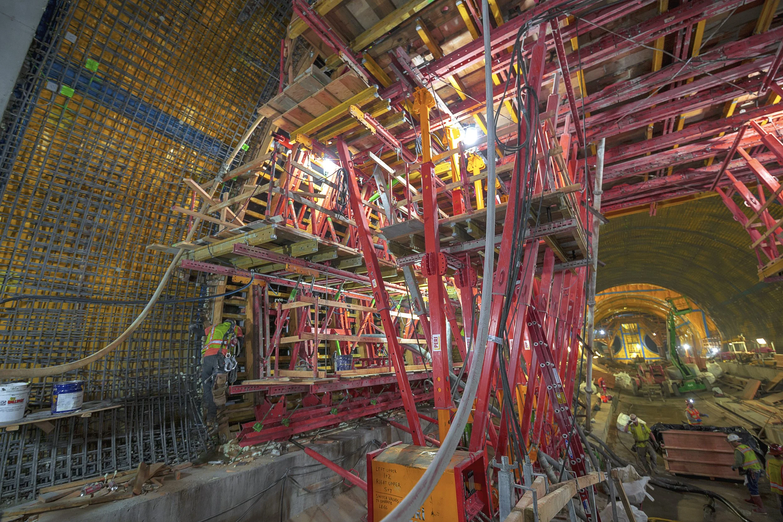 Construction workers inside a tunnel building scaffolding, with various tools and materials around.