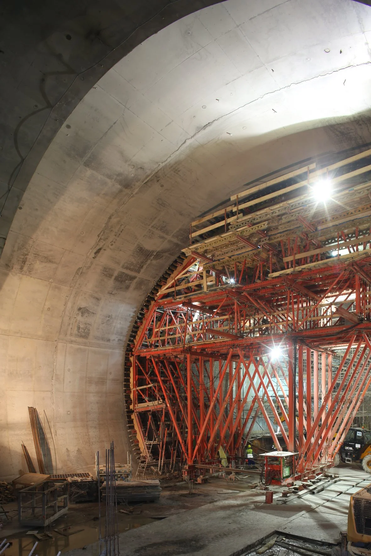 Construction site inside a tunnel with red scaffolding and workers.