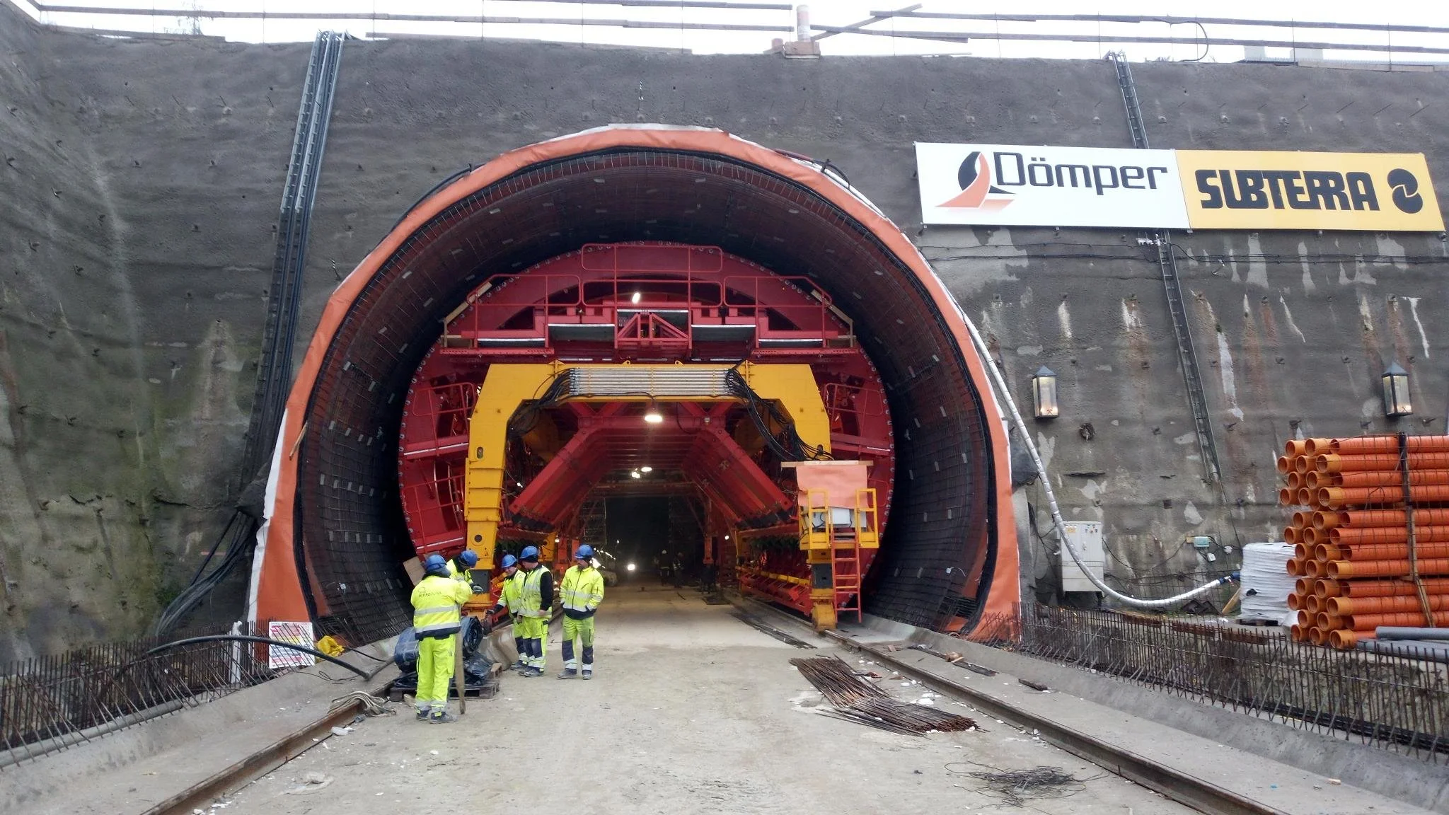 Construction workers in safety vests and helmets standing in front of a large tunnel boring machine at a construction site.
