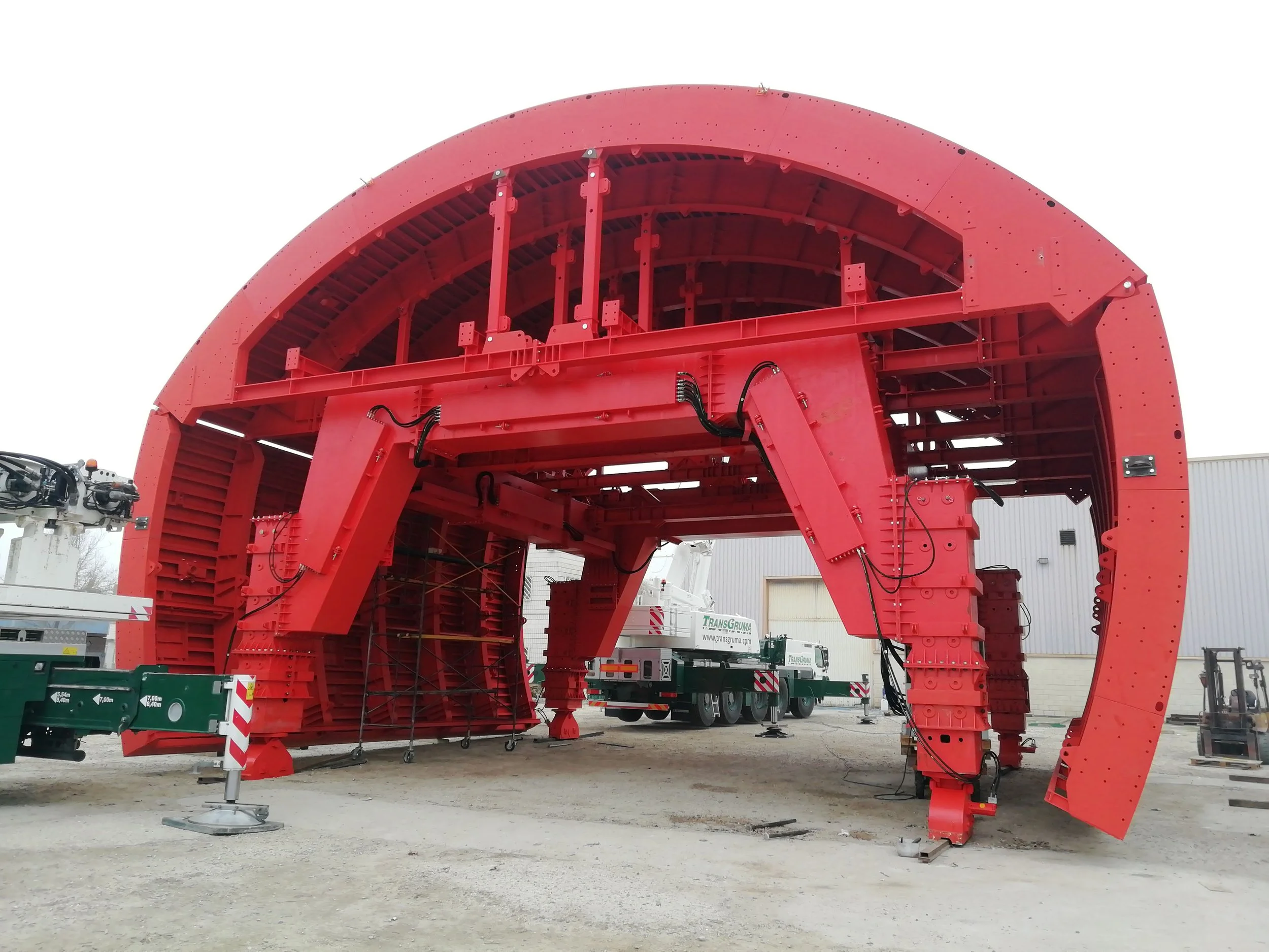Large red industrial structure with scaffolding and machinery outside a warehouse.