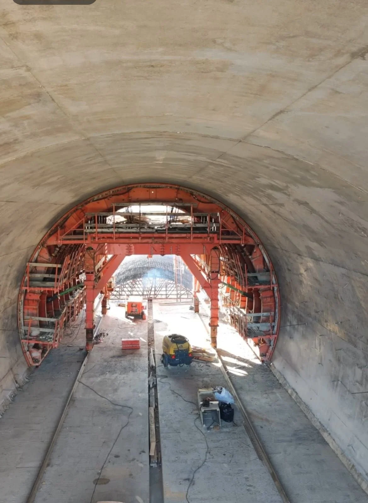 Construction site inside a tunnel, with scaffolding and construction equipment, and train tracks laid on the ground.