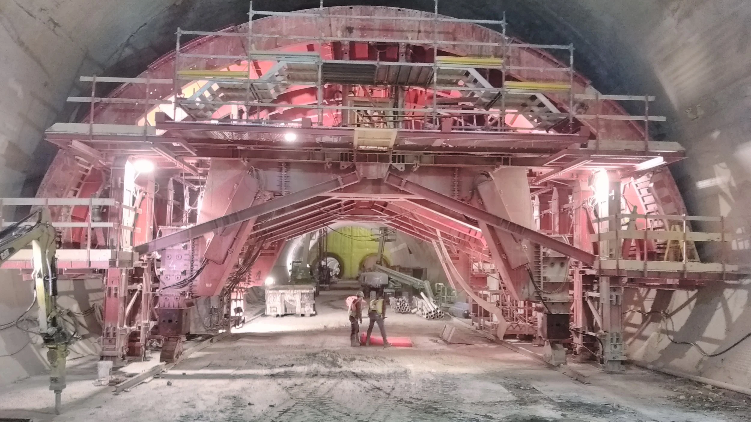 Under construction tunnel with large machinery and scaffolding, two workers inspecting the area.