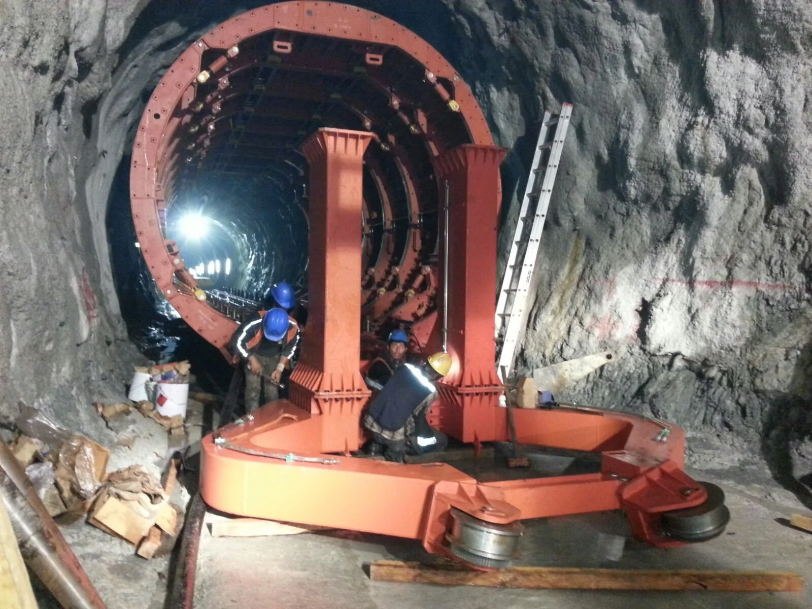 Workers wearing safety helmets and reflective vests assembling or maintaining a large tunnel boring machine inside an underground tunnel under construction.