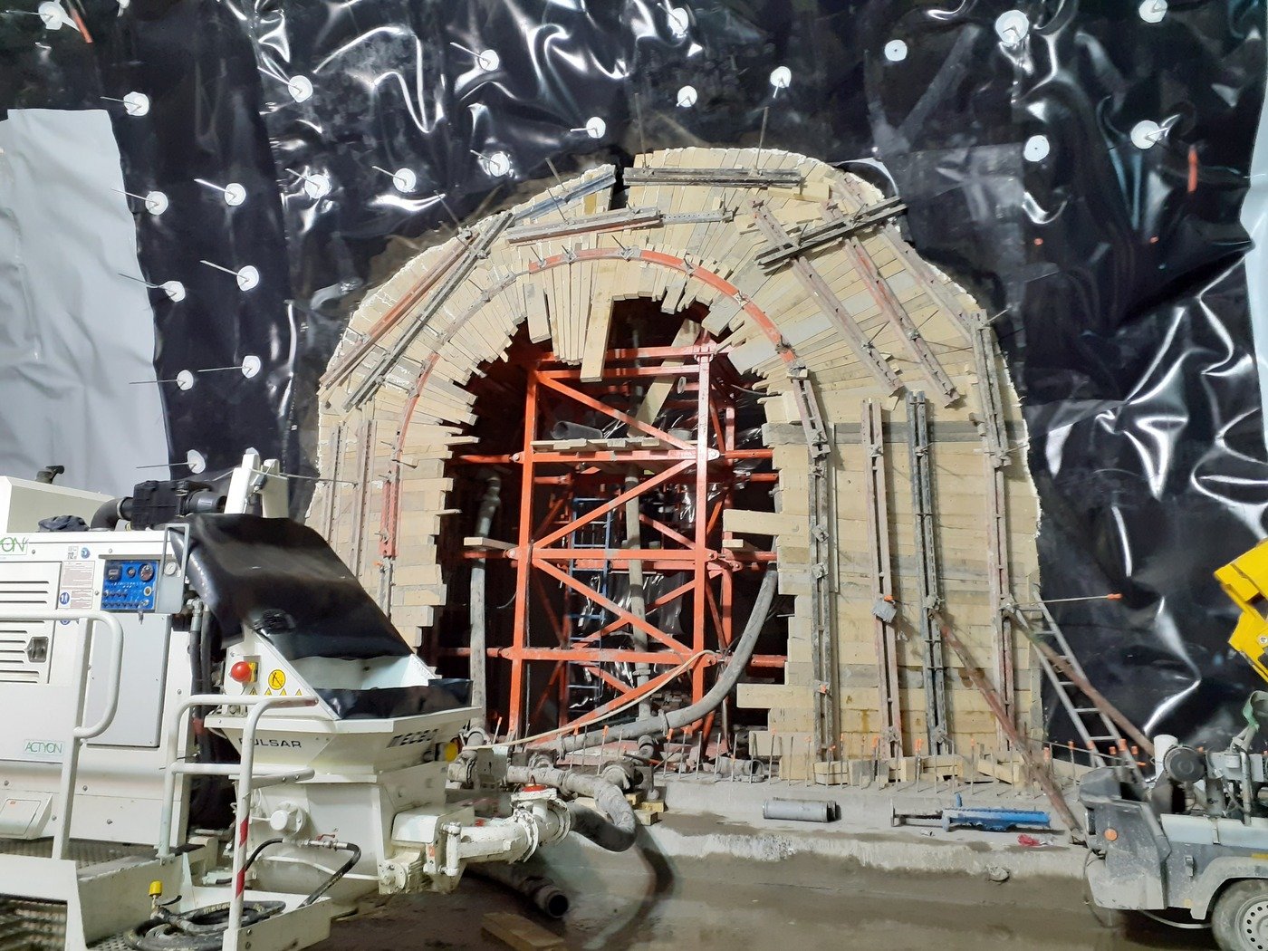 Undergoing construction or renovation of a tunnel or archway, with scaffolding, wooden and metal supports, and construction equipment, surrounded by black plastic sheeting.