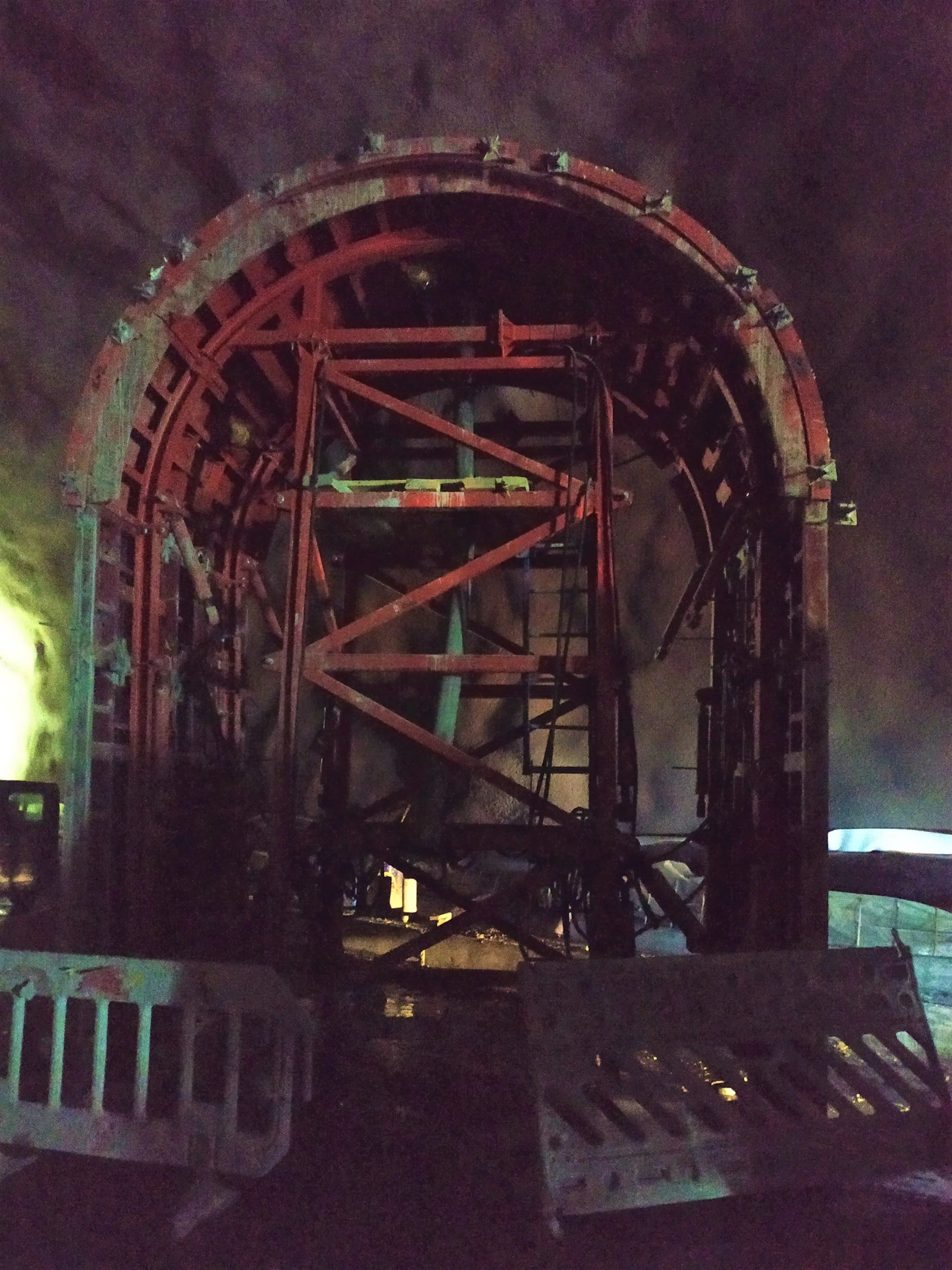 Damaged roller coaster structure at night, with a large circular section and red support beams, surrounded by smoke or fog.