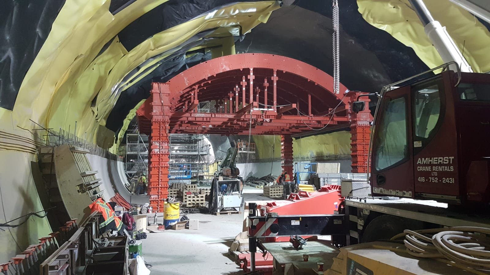 Construction workers building a tunnel with scaffolding and equipment inside a large underground tunnel.