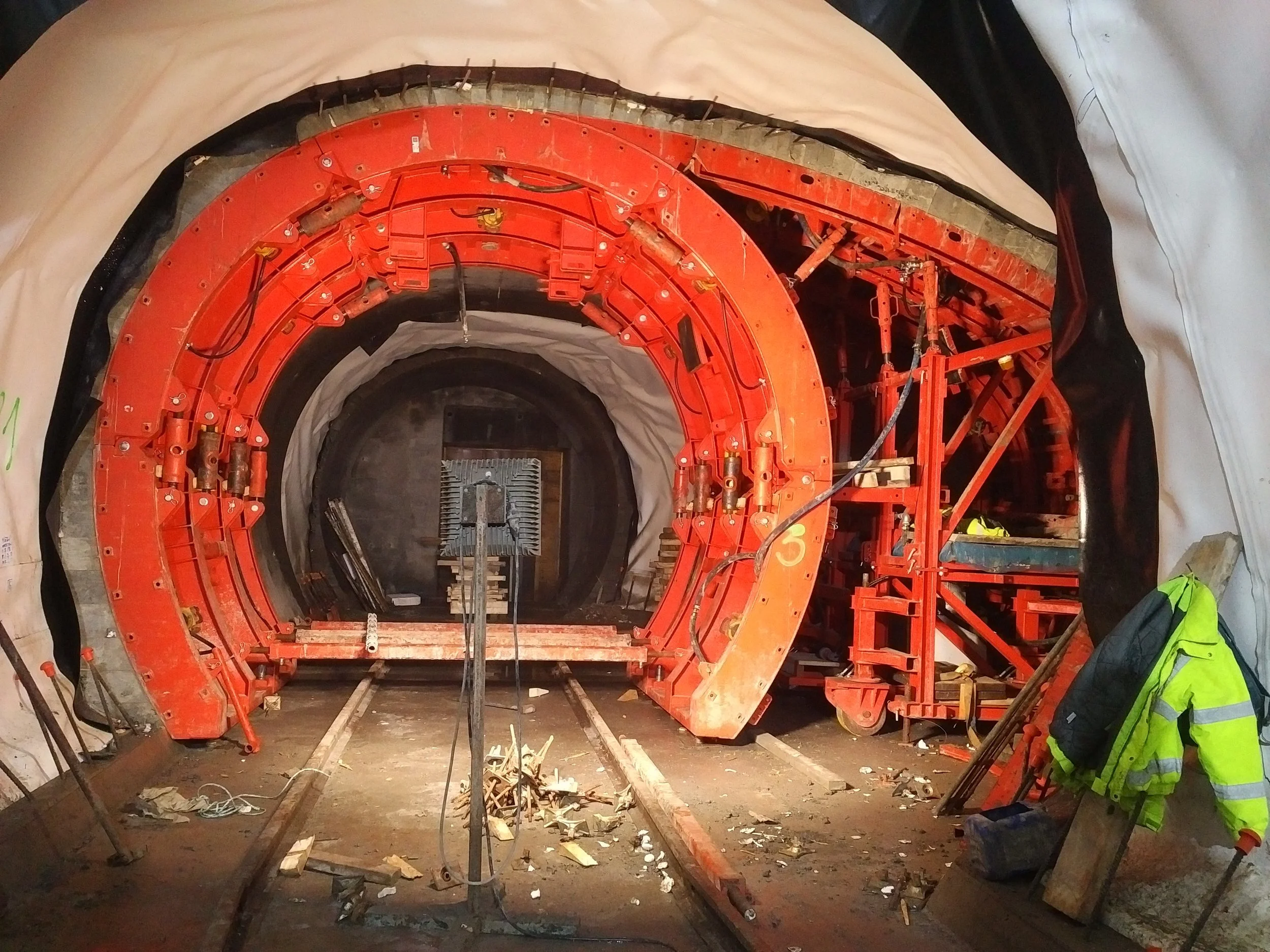 Construction site inside a tunnel with red machinery, safety equipment, and construction tools.