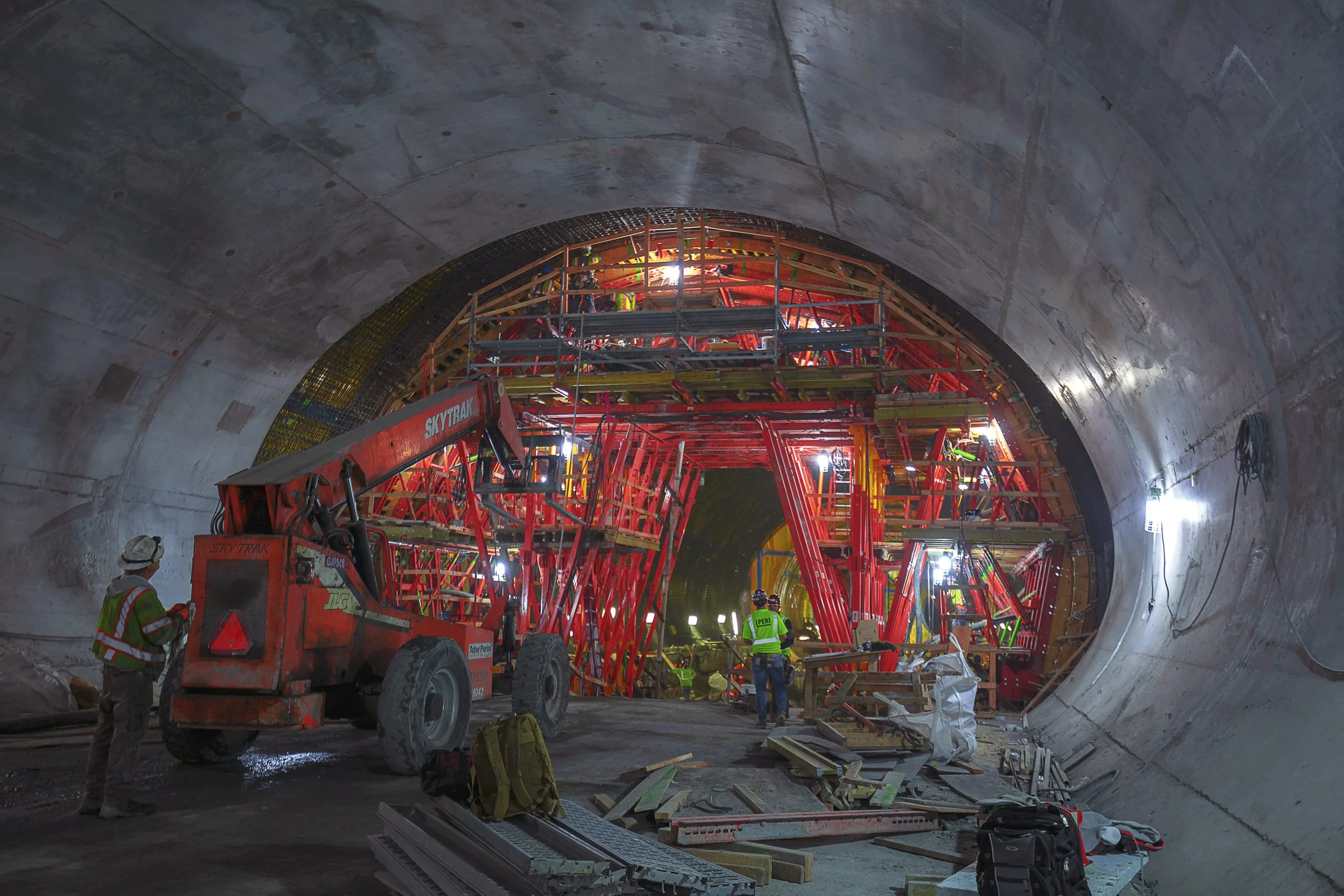 Construction workers in a tunnel, with equipment and scaffolding, working on the interior tunnel lining.