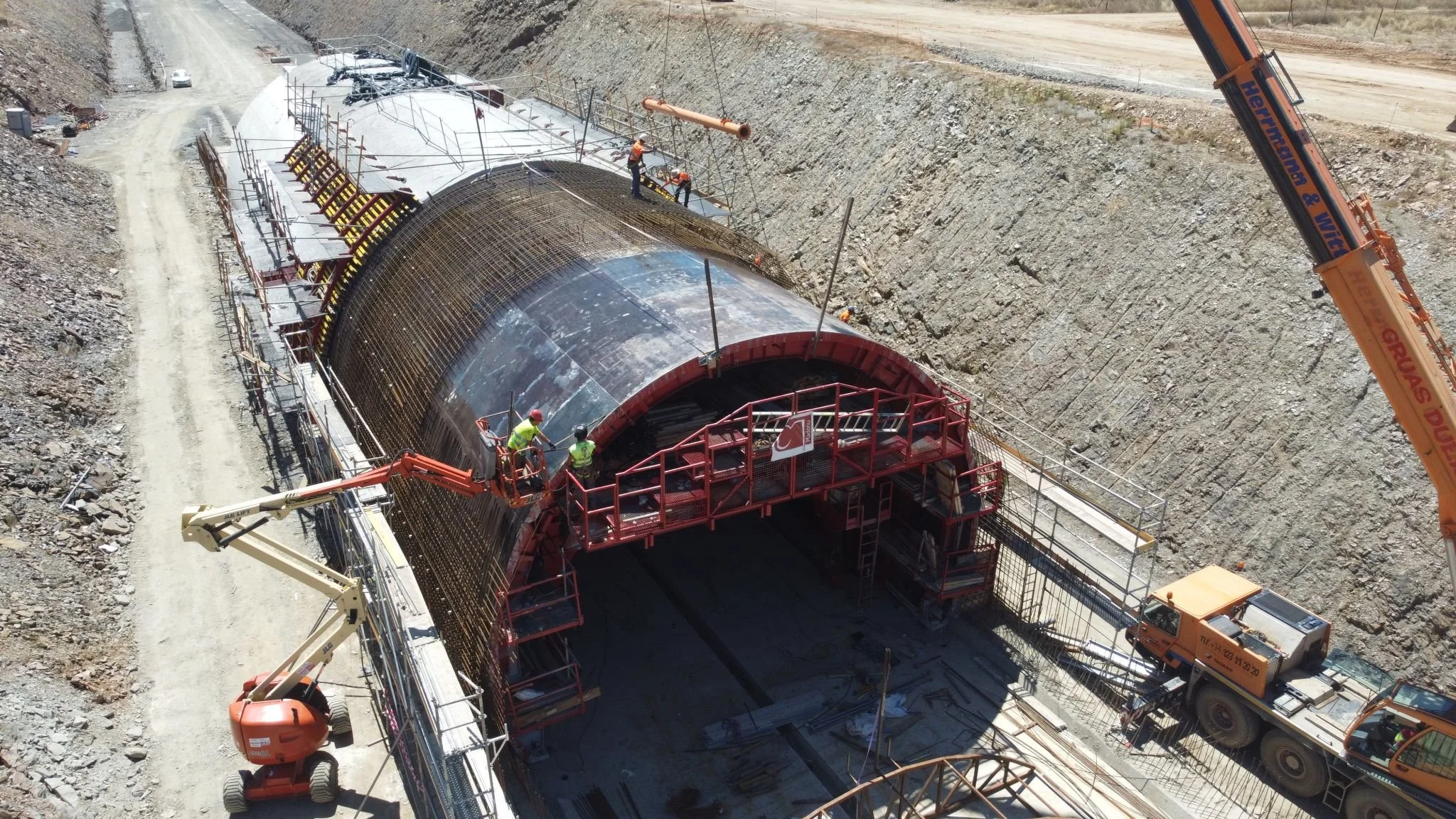 Construction workers and machinery working on a tunnel under construction, with a large crane and a boom lift nearby.