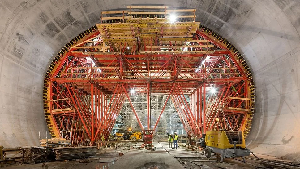 Construction workers inside a large underground tunnel with extensive scaffolding and support structures.