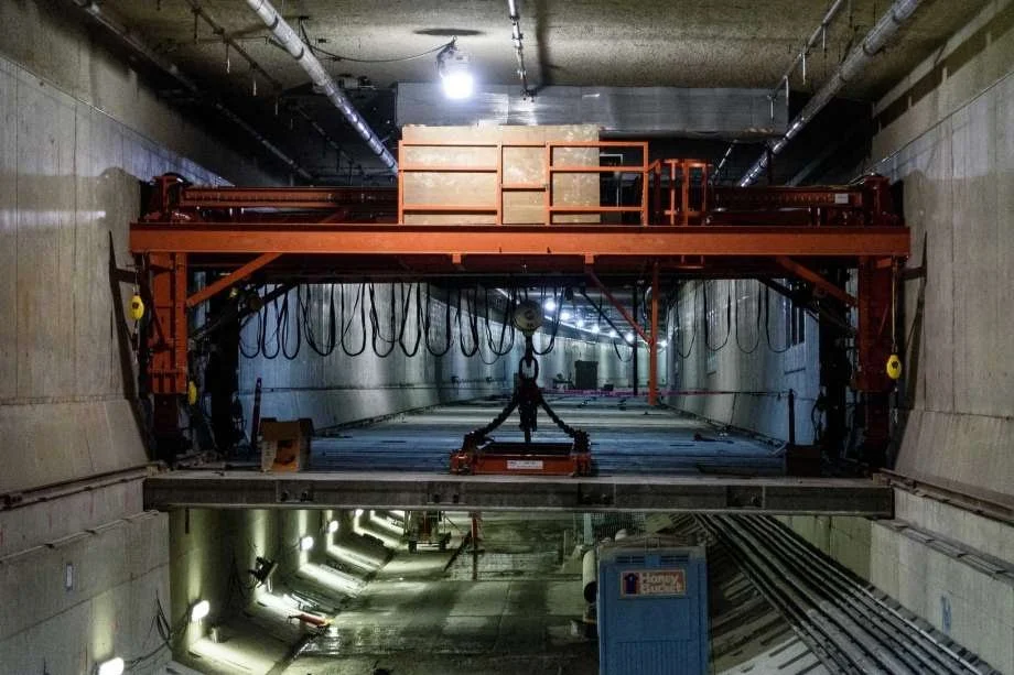 Construction worker in a tunnel operating a large red tunnel boring machine with various equipment and lighting.