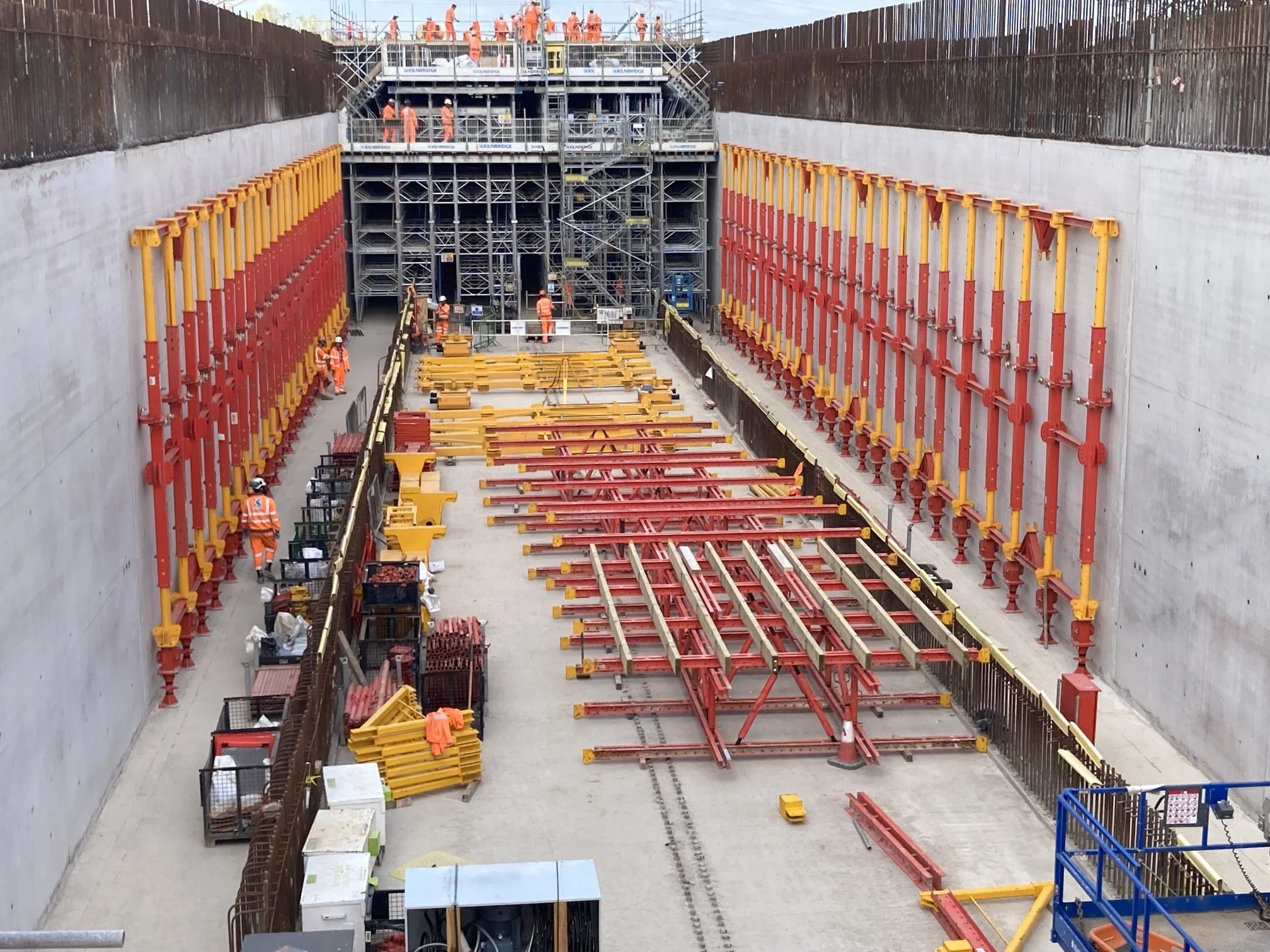 Construction workers building a tunnel with support beams and scaffolding inside a large excavation site.